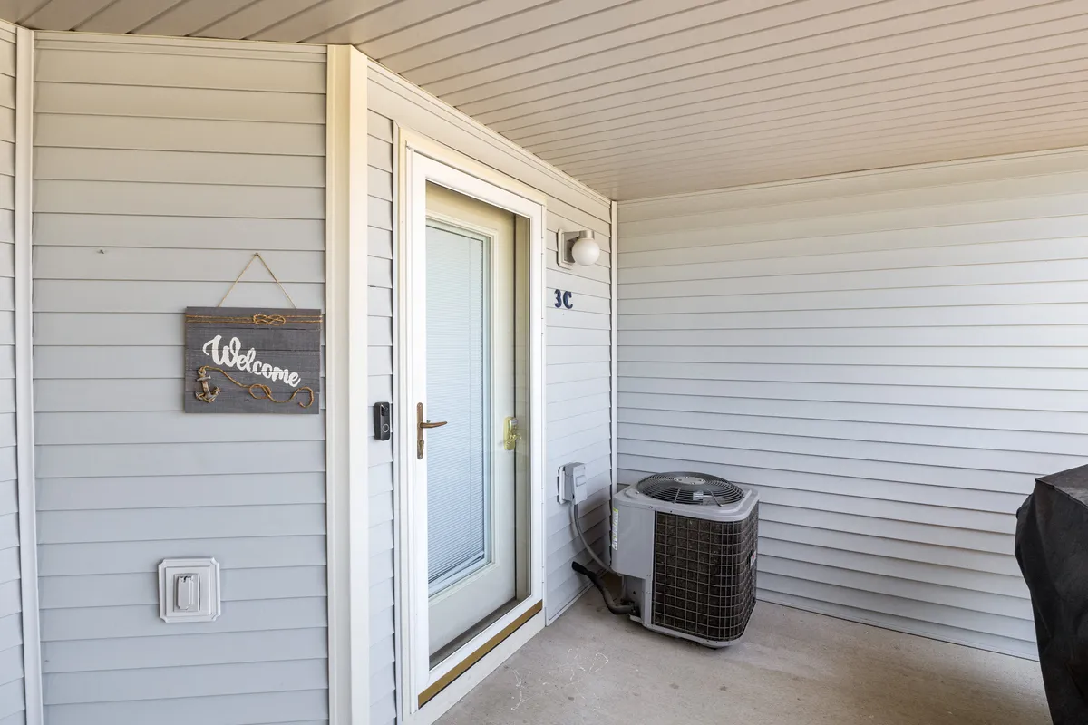 A welcoming entryway featuring a secure front door with a prominent welcome sign and visible air conditioning unit. The scene is bright and inviting, suggesting a secure and comfortable arrival experience enhanced by smart access technology.