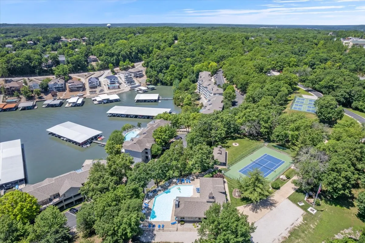 A vibrant exterior scene featuring a swimming pool, tennis courts, a marina, and lush greenery. The image captures multiple amenities in one frame, emphasizing the opportunities for active, multi-generational recreation—swimming, boating, tennis, and relaxing by the pool, all set against a picturesque lake backdrop.