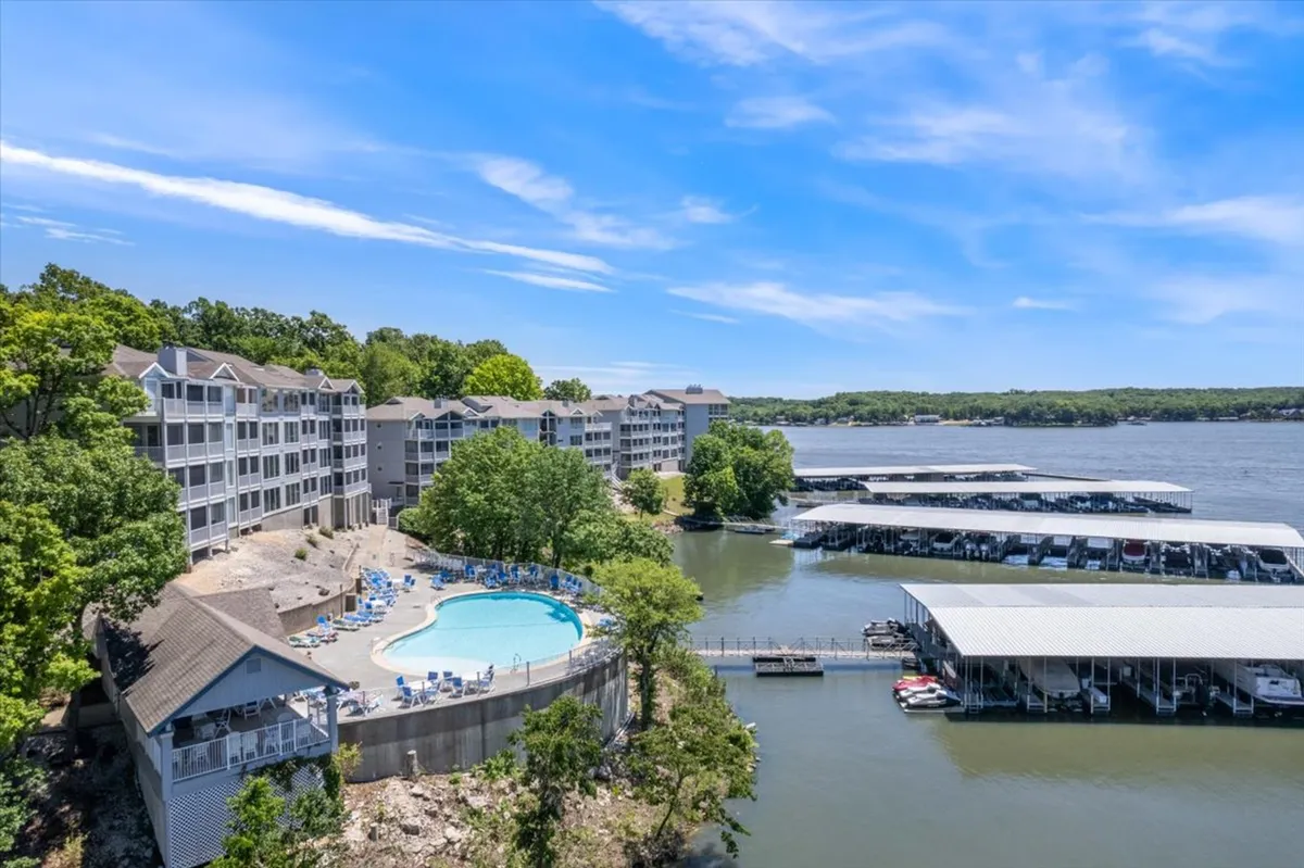 A scenic swimming pool overlooking a marina filled with boats, surrounded by trees and a residential complex. The pool area invites relaxation and socializing, while the marina hints at more lake adventures just steps away.