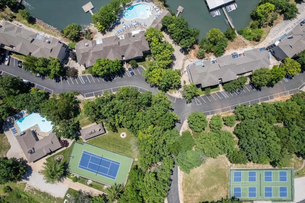 This exterior image features multiple swimming pools, a tennis court, waterfront views, and green spaces with visible parking areas. The scene is lively and suggests a hub of outdoor activity, offering clear glimpses of the recreational spaces available to guests.