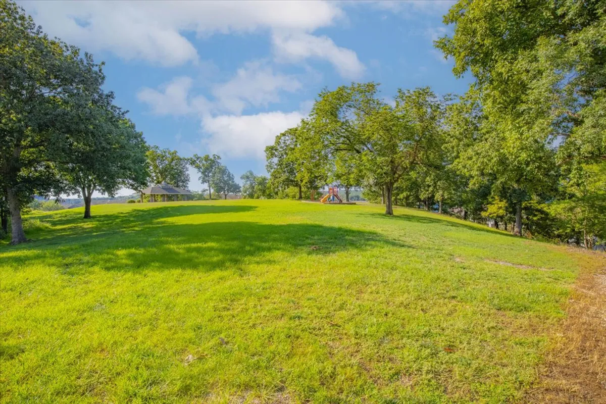 A vibrant, open park area featuring lush green grass, a modern playground with equipment for children, shade trees, and a pavilion for gatherings. Families and children can be imagined playing and spending time together in the fresh air.