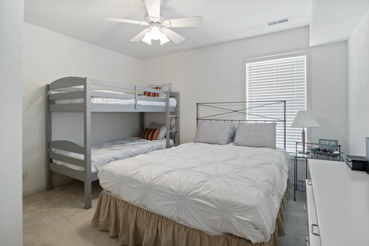 A family-friendly bedroom setup with a bunk bed and a queen bed, complemented by a nightstand and playful decorative pillows. The arrangement suggests comfort for groups, families, or friends sharing the space, and the relaxed mood hints at cozy nights and shared stories.