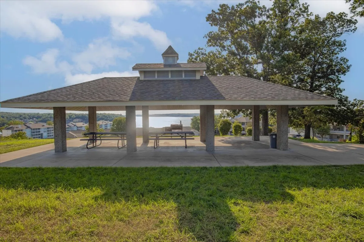 The photo captures a lakeside pavilion surrounded by trees with sweeping views of the water. The atmosphere is relaxed and inviting, ideal for group picnics or watching the sunset after a day on the lake.