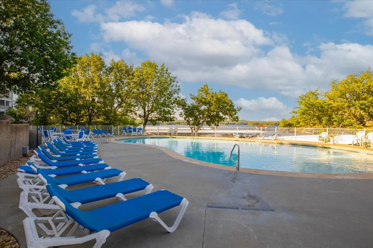 A serene outdoor pool surrounded by lounge chairs and lush trees, basking in the warm glow of sunset. The tranquil water reflects the sky, inviting residents to relax, sunbathe, or enjoy a quiet swim. The area exudes a peaceful, resort-like ambiance.